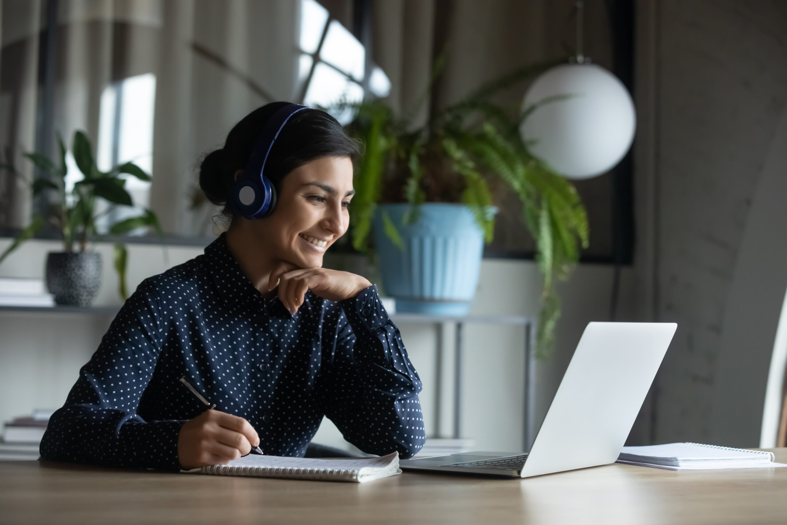 Happy young indian girl with headphones looking at laptop screen.